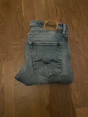 Replay Thad ljusblå jeans straight fit - Säljer ett par Replay Thad jeans i ljusblå tvätt med snygga slitningar och klassisk femficksdesign. Jeansen har raka ben och normal passform, med Replay-logga på bakfickan och läderpatch i midjan. Perfekt för dig som gillar en avslappnad stil.
