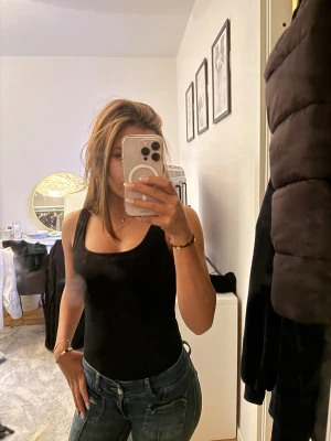 Svart ärmlös linnebody från H&M - Svart, enkel och tight linnebody från H&M med breda axelband och rundad halsringning. Gjord i mjuk bomullsmix som sitter skönt mot kroppen. Perfekt att styla med jeans eller kjol för en clean look.