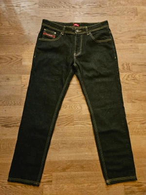 Ecko Unltd. Jeans - Snygga mörkblå jeans från Ecko Unltd. i straight fit-modell. Byxorna har tydliga gula kontrastsömmar, klassiska fem fickor och coolt logobroderi på bakfickan. Bra skick. Storlek 32/32. Mått: Midja 41 cm Front rise 25 cm Lår 27 cm Innersöm 73.5 cm  Yttersöm 99 cm Benöppning 16 cm