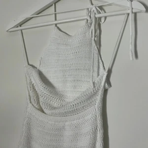 Vit virkad långklänning med knyt - Superfin vit virkad långklänning med smala axelband och knyt i nacken. Klänningen är ärmlös och har en lätt vågig struktur i materialet. Perfekt för varma dagar och ger en chill boho-vibe.
