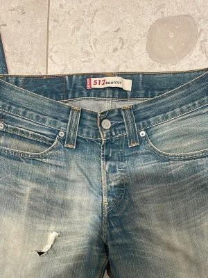 Levis ljusblå bootcut jeans - Säljer ett par klassiska Levis jeans i ljusblå tvätt med bootcut passform. Jeansen har låg midja, fem fickor och ett snyggt slitet hål på låret för en extra edge. Tillverkade i robust denim som ger en avslappnad vibe.