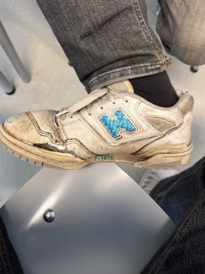 Vita sneakers med blå detalj och smiley (pewdipies gamla skor) - Unika vita sneakers med blått holografiskt märke på sidan och handritad grön smiley framtill. Skon har snörning, perforerade detaljer och texten 'Pitcha' skrivet på sidan. Tillverkad i skinnliknande material och har en klassisk rund tå.