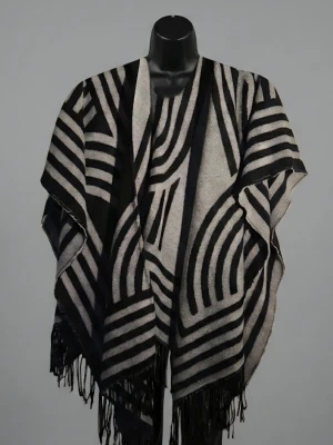 Svart och grå poncho - Säljer en snygg poncho i svart och grått med grafiskt randigt mönster. Ponchon har öppet framtill och långa fransar längs nederkanten. Perfekt att slänga över en outfit för extra stilpoäng. Materialet känns mjukt och stickat.