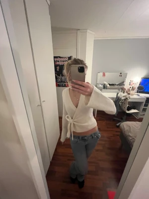 Vit omlottkofta med knyt - Säljer en superfin vit omlottkofta med knyt i sidan. Tröjan är croppad och har långa ärmar samt en djup v-ringning. Perfekt att styla med jeans eller kjol för en trendig look. Materialet känns mjukt och är stickat.