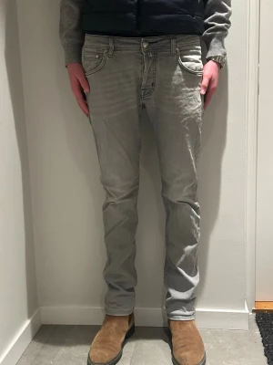 Grå jeans från Jacob Cohen - Säljer ett par grå jeans från Jacob Cohen med klassisk femficksdesign och knappgylf. Jeansen har en rak passform och är tillverkade i mjukt bomullsmaterial. Modellen är 184 cm lång, hör av er vid frågor 😀