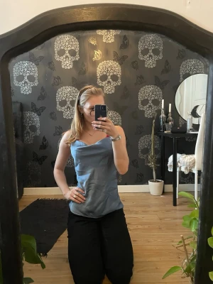 Blå linnetopp från VILA - Säljer en stilren blå linnetopp från VILA i satinliknande material. Toppen har tunna axelband och en snygg draperad urringning. Perfekt att matcha med jeans eller kjol för en trendig look.