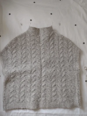 Grå stickad ärmlös tröja White Stuff - Supermysig grå stickad tröja från White Stuff i storlek S. Tröjan är ärmlös med hög krage och har ett snyggt flätmönster över hela. Perfekt att slänga på över en långärmad topp eller ba anväda som t-shirt. 