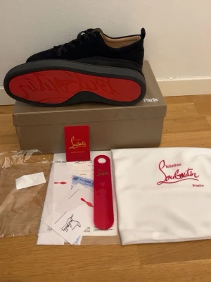 Christian Louboutin svarta sneakers - Säljer ett par svarta sneakers från Christian Louboutin med ikonisk röd sula och snygga detaljer. Skorna är gjorda i mocka med snörning och har en platt sula. Innersulan är i beige skinn med guldfärgad logga. Kommer med originalkartong och dustbag.