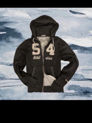 Abercrombie & fitch zip - Mörkgrå hoodie med dragkedja från Abercrombie & Fitch | Stor broderad 54 och texten Athletics framtill, vita snören i huvan och fickor på magen | Size M, passar M | Smådefekter kommer men ska vara så för vintage stil