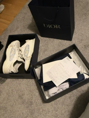 Vita Dior sneakers b30’s - Säljer ett par exklusiva vita Dior sneakers med reflekterande detaljer på sidorna och tydlig Dior-logga. Skorna har snörning, rund tå och en chunky sula. Materialmix av skinn och mesh ger både stil och komfort. Måste säljas snabbt därav priset. Tveka inte att skriva vid minsta lilla fundering. Pris kan diskuteras vid snabb affär