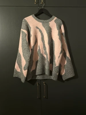 Grå och rosa stickad tröja zebra - Säljer en oversized stickad tröja i grått och ljusrosa från Indiska med zebramönster. Tröjan har rund halsringning, långa ärmar och ribbade muddar. Ej använd någon gång och är slutsåld produkt!