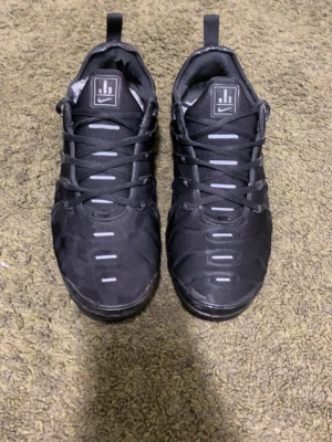 Nike Air Vapormax Plus svarta sneakers - Säljer ett par svarta Nike Air Vapormax Plus. Strl 42. Några småfel men som inte syns så mycket. Bra skick.