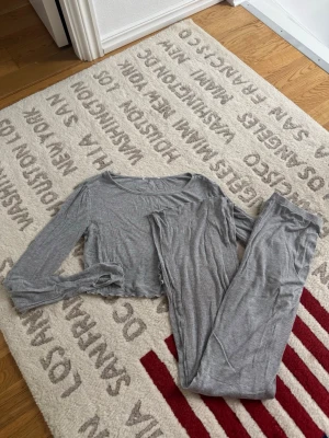 Grå ribbad lounge set - Säljer en grå ribbad set i mjukt och stretchigt material. Byxorna och tröjan har en croppad passform, långa ärmar med tumhål och diskreta vågiga kanter. Perfekt för en chill och avslappnad stil.