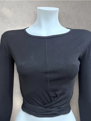 Hope  långärmad topp med knyt -  svart långärmad topp från Hope. Toppen har rund halsringning, markerad söm framtill och långa band i midjan som kan knytas på olika sätt för en snygg twist. Modellen är croppad och har en liten slits framtill. #hope #topp #croppad