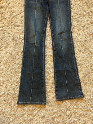 Bootcut jeans från Madlady, blå 32/reglar - Säljer ett par blå bootcut jeans från Madlady i klassisk denim med markerade sömmar och dubbla knappar i midjan. Jeansen har framfickor och bakfickor med lock och knappdetalj. Snygg tvätt och skön passform, perfekta till sneakers eller boots. De är köpta för ungefär 800kr och är i princip oanvända, är i storlek 32 reg💗💗