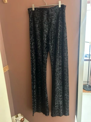 Svarta paljettbyxor från Zara - Glittriga svarta byxor från Zara, täckta med paljetter för maxad partykänsla. Byxorna har hög midja och ett rakt, lite vidare ben som ger en snygg siluett. Stretchigt material som gör att de sitter perfekt! Perfekt för längre då jag är 174 och de är långa på mig i benen. 
