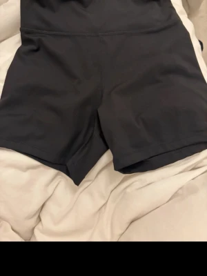 Svarta träningstights-shorts MOVE - Säljer ett par svarta träningstights-shorts från MOVE. De är högmidjade och har en tight passform som sitter skönt vid träning. Materialet är stretchigt och känns som syntet, perfekt för gymmet eller löprundan.