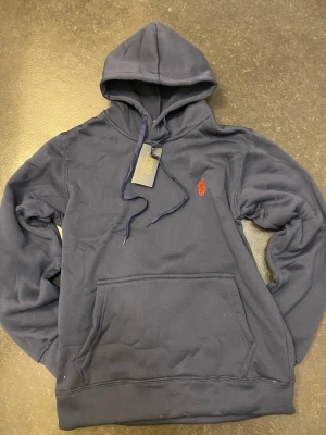 Polo Ralph Lauren blå hoodie - Stilren blå hoodie från Polo Ralph Lauren med klassisk logga på bröstet. Mjuk och bekväm passform, perfekt till vardags. Storlek-S.