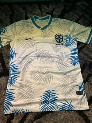 Brasil fotbollströja - Bilderna visar en Brasilien fotbollströja från Nike med blått och grått palmbladsmönster.