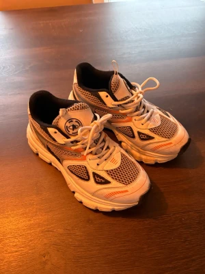 Arigato sneakers - Säljer ett par Axel Arigato skor. Skorna är vita med orange detaljer. Perfekt för den som söker ett par bekväma och stilrena skor. Storlek 38! Knappt använda så väldigt bra skick. Säljer för 1500kr
