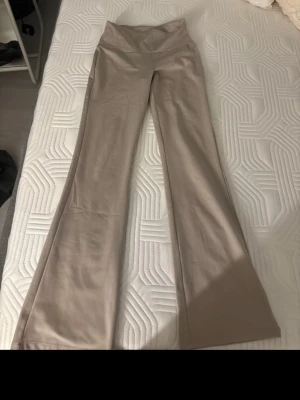 Beiga bootcut byxor med hög midja - Säljer ett par snygga beiga byxor med bootcut och hög midja. Byxorna är i tränings material, perfekta för en chill och trendig look. Passformen är figurnära upptill och vidare nedtill, vilket ger en riktigt schysst siluett. 