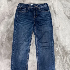 Blå jeansbyxor från Lindex - Snygga blå jeansbyxor från Lindex med klassisk femficksdesign och kontrastsömmar. Modellen har rak passform och resår i midjan baktill för extra komfort. Perfekt för dig som gillar enkel och tidlös stil.