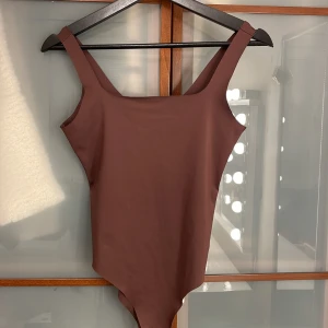 Brun body från Zara - Snygg brun body från Zara i storlek medium. Modellen har breda axelband och en stilren, enkel design med fyrkantig ringning.