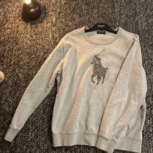 Ralph lauren sweatshirt  - Snygg grå sweatshirt från Polo Ralph Lauren med stort broderat polospelare-logo på bröstet. Tröjan har rund hals, långa ärmar och ribbade muddar vid ärmslut och nederkant. Perfekt för en chill och stilren look.