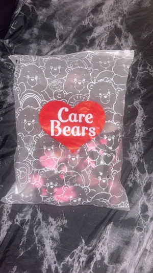 Care Bears pyjamas set med rosa nallemönster - Supergullig pyjamas från Care Bears i storlek S med svart botten och rosa nallebjörnar, stjärnor och hjärtan över hela tyget. Toppen har smala axelband och byxan är i shortsmodell. Materialet är mjukt och stretchigt, 90% polyester och 10% elastan. Perfekt för dig som älskar söta prints!