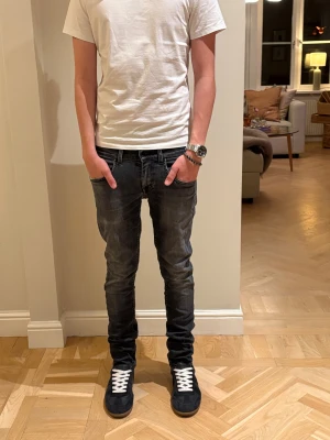 Feta svarta jeans - Snygga mörkgrå jeans med smal passform och klassisk femficksdesign. Jeansen har diskreta slitningar och kontrastsömmar, vilket ger en cool och modern look. Perfekta för dig som gillar en smal siluett och streetstyle.