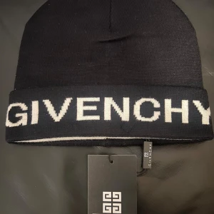  Givenchy Mössa - Snygg svart och vit mössa från Givenchy med stor logotyp i vitt framtill. Mössan är stickad och har en klassisk, rundad form med uppvikt kant. Perfekt för dig som vill ha en lyxig och trendig accessoar med tydlig designerstil.