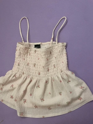 Blommig ljusrosa linnetopp Gina Tricot - Supersöt ljusrosa linnetopp från Gina Tricot i storlek XS. Toppen har smala axelband, smockad överdel och ett blommigt mönster med små rosa och gröna blommor. Materialet är mjukt och lätt, perfekt för varma dagar. Passformen är normal och toppen är ärmlös.