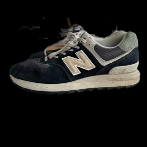 New Balance sneakers i mörkblå mocka - Snygga New Balance sneakers med mörkblå mocka och mesh, beige detaljer och klassisk N-logga på sidan. Skorna har rund tå, platt sula och snörning. Perfekt för dig som gillar retrostil och vill ha bekväma sneakers med cool design. Hör av dig om fler bilder eller funderingar.