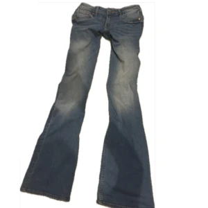 Blå bootcut jeans från Levi's - Snygga blå jeans från Levi's med klassisk bootcut-passform och låg midja. Jeansen har fem fickor, slitningar och ljusare tvättade partier på benen för en cool look. Perfekta för dig som gillar retrostil och vill ha ett par jeans med lite extra attityd.