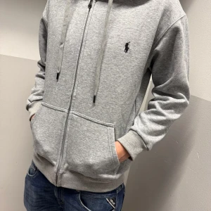 Grå hoodie från Polo Ralph Lauren - Säljer denna feta Raulph Lauren zip up hoodien. Den är galet skön inuti och helt nytt skick. Lappen sitter kvar. Modellen är 177 cm lång. Tröjan är M men passar mer S. Priset kan diskuteras vid snabb affär. 