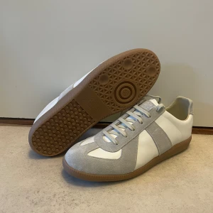 Maison Margiela sneakers i vitt och grått - Säljer ett par helt oanvända Maison Margiela i storlek 42. Säljer på grund av fel storlek. Nypriset ligger på ungefär 7000kr!! Tyvärr ingen skolåda, därav priset!!! Skicka DM om du vill ha fler bilder!! OBS! Färgerna på bilderna är ljusare i verkligheten, likt bild 5.