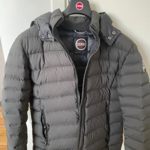 Colmar jacka - Säljer en svart pufferjacka från Colmar med huva och snygga horisontella sömmar. Jackan har dragkedja framtill och två praktiska fickor med dragkedja. Perfekt för kalla dagar och har en stilren look som funkar till det mesta. Jackan är inköpt förra vintern men har knappt använts. Storlek 50 som motsvarar typ S/M