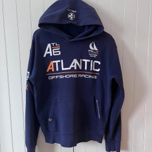 Rare Ralph lauren hoodie  - Snygg marinblå hoodie från RLX Ralph Lauren med tryck i vitt och orange på bröstet och ärmen. Tröjan har stor huva, känguruficka och coola offshore racing-detaljer. Perfekt för dig som gillar sportig och avslappnad stil. Säljs inte längre och är sjukt limiterad så först till kvarn!