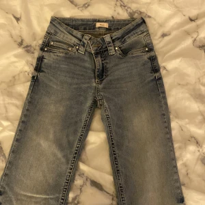 Blå jeans från Nelly med broderade fickor - Snygga helt nya och oanvända  blå jeans från Nelly med klassisk femficksdesign och coola broderade bakfickor med knappar. Jeansen har normal passform, låg midja och är tillverkade i jeansmaterial med slitningar för en trendig look.