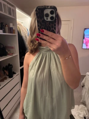 Glittrig ljusgrön halterneck topp från Zara - Säljer en superfin ljusgrön halterneck topp från Zara med glittrigt tyg. Toppen har en hög hals och är ärmlös, med ett flowy och luftigt fall. 