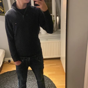 Mörkblå half zip tröja Tommy Hilfiger - Snygg mörkblå långärmad tröja från Tommy Hilfiger med half zip och liten broderad logga på bröstet. Tröjan har ribbade muddar och krage, tillverkad i mjuk bomull som känns skön mot huden. Perfekt för dig som gillar att använda klassiska  och stilrena plagg.