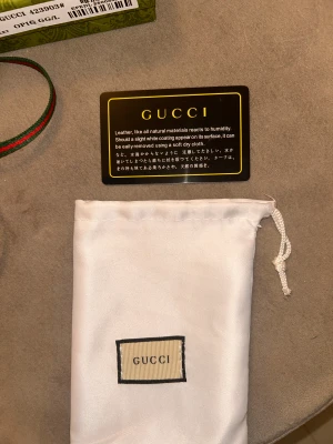 GG plånbok med orm och GG-mönster - Snygg plånbok från GG med klassiskt GG-mönster i beige och brunt, dekorerad med en cool röd, vit och svart orm på framsidan. Plånboken har dragkedja, flera kortfack och en grön-röd rem. Kommer med original ask och dustbag.