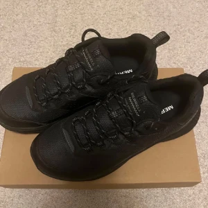 Svarta sneakers från Merrell - Säljer ett par svart sneakers från Merrell. Skorna har en robust design med snörning och en slitstark sula, perfekt för utomhusaktiviteter. De är helt svart och har en bekväm passform. Skorna har bara använts 1 gång.