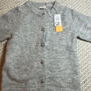 Ljusgrå stickad kofta med knappar - Säljer en ljusgrå stickad kofta från Y i storlek 146/152. Koftan har rund hals, långa ärmar och snygga pärlknappar framtill. Perfekt för lager-på-lager och chill dagar. Mjuk och skön känsla tack vare det stickade materialet.