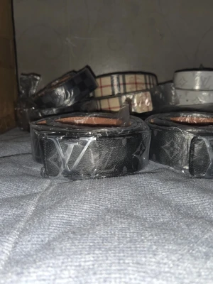 Svart Louis Vuitton bälte med monogram - Snyggt svart bälte från Louis Vuitton med klassiskt monogrammönster och silverfärgat LV-spänne. Bältet har en stilren design och är tillverkat i ett slitstarkt syntetmaterial med läderlook. Perfekt för att lyfta din outfit med en exklusiv touch.