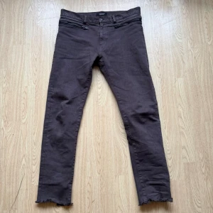 Undercover Slim fit jeans - Säljer ett par jeans från Undercover Jun Takahashi med råa, fransiga benslut och två grova dragkedjor framtill. Färgen betecknas grå men går mer åt det bruna hållet.  Jeansen har klassiska bakfickor och är gjorda i ett slitstarkt bomullsmaterial. Perfekt för dig som gillar detaljer och streetwear. Storlek 5 (33”-34”)