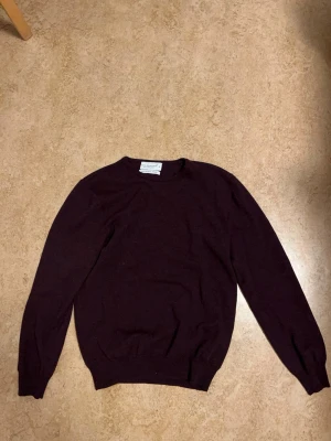 Mörk vinröd merinoullströja Cedar Wood State - Säljer en stilren mörk vinröd tröja från Cedar Wood State i storlek L, tillverkad i 100% merinoull. Tröjan har rund hals, långärmad design och ribbade muddar vid ärmslut och nederkant. Perfekt för dig som gillar klassisk och enkel stil.