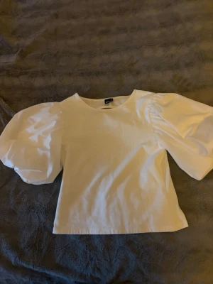 Vit blus med puffärmar och öppen rygg - Supersnygg vit blus från Gina med stora puffärmar och rundad öppen rygg. Använd en gång. Ganska liten i storleken, skulle passa S. 