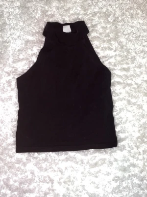 Svart polotopp i bomull från ginatricot stl S - Säljer en svart polotopp i mjuk bomull med ärmlös design och hög krage. aldrig använd, löparen betalar frakt☺️