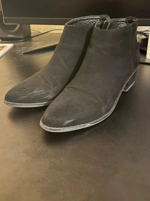 Svarta stövletter med klack, storlek 40 - Säljer ett par svarta stövletter från DSY i storlek 40. Skorna har spetsig tå, låg klack och dragkedja på sidan för enkel på- och avtagning. Yttermaterialet är mocka och insidan är fodrad med syntet. Perfekt till dig som gillar stilrena boots med lite edge.